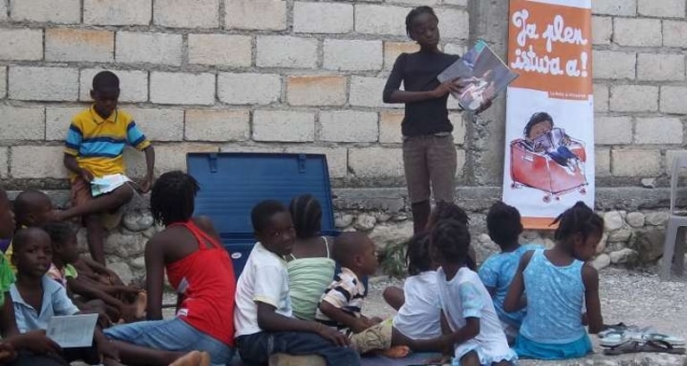 Photo d'une jeune réfugiée lisant un livre à ses camarades à Port-au-Prince