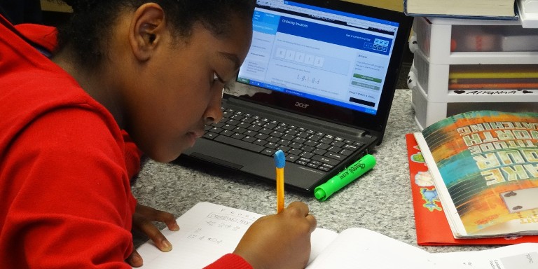 Photo d'une petite fille avec un cahier et la khan academy sur son ordinateur