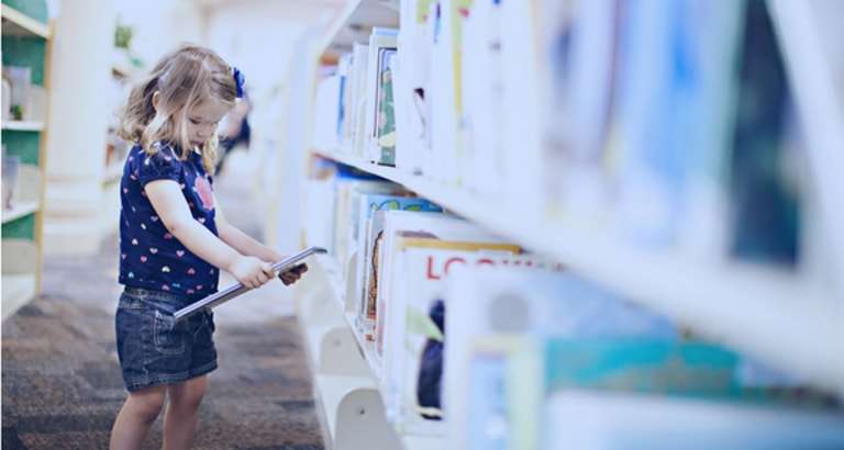 Photo d'une petite fille regardant un livre dans une bibliothèque