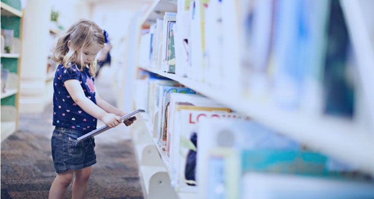 Photo d'une petite fille regardant un livre dans une bibliothèque